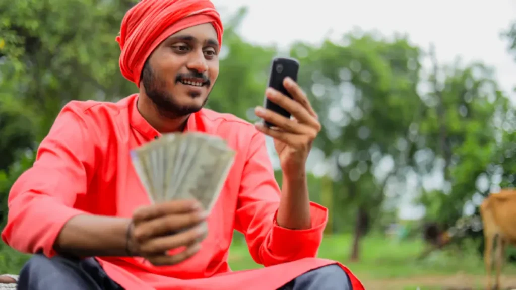 Indian farmer checking PM Kisan instalment status on mobile while holding money in hand.